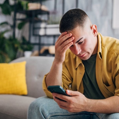 A stressed man sitting on a couch looking at his phone