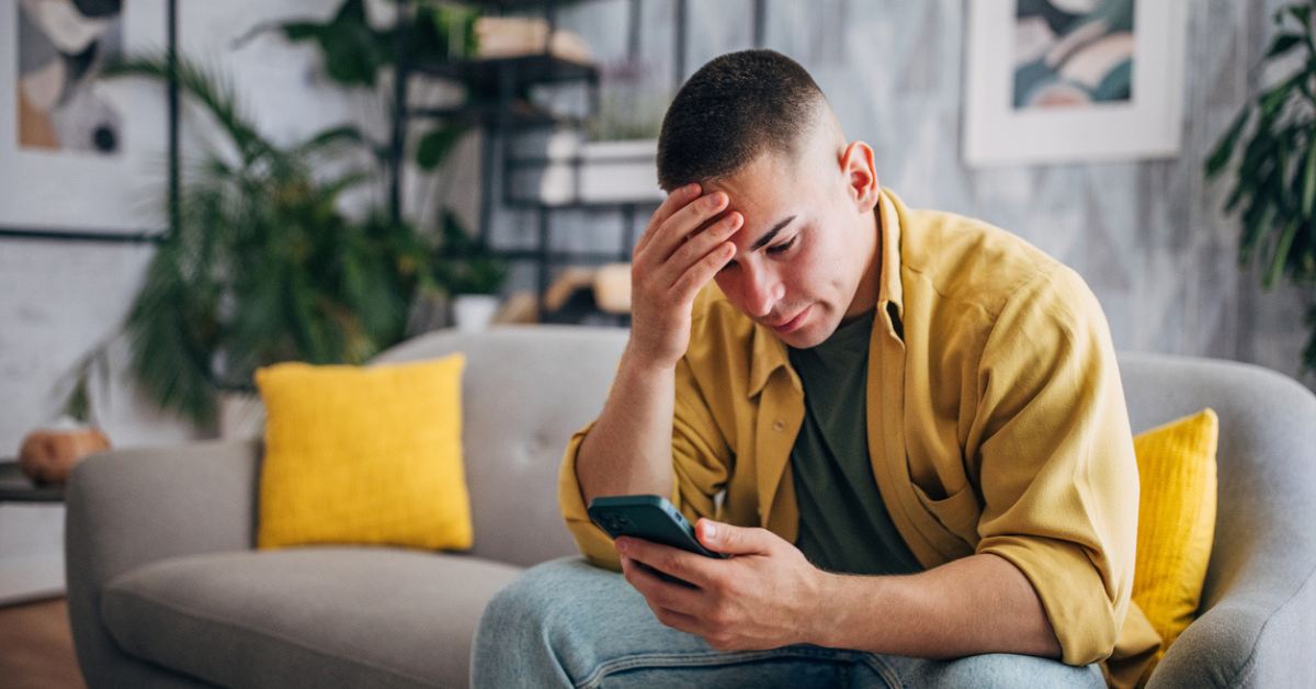 A stressed man sitting on a couch looking at his phone